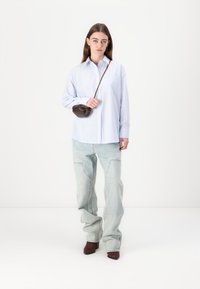 Lyseblåstripet skjorte med knapper, oversized passform, med brystlomme. Lysvaskede baggy jeans. Brun miniveske med skulderrem. Brune hælstøvler.