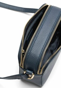 Petit sac bandoulière en cuir bleu marine avec deux fermetures éclair dorées ouvertes et une fine bandoulière réglable sur fond blanc.