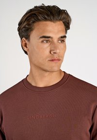 Mörkröd sweatshirt med rund halsringning, med ett präglat "LINDBERGH"-logotyp på bröstet och ett slätt, texturerat tyg.