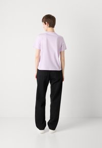 Camiseta de manga corta de color púrpura claro combinada con pantalones negros de corte ancho, con un diseño sencillo y una textura suave y lisa.