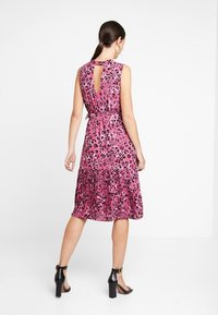 Rosa ärmelloses Kleid mit schwarzem Leopardenmuster, plissiertem Rock, ausgestanztem Detail am Rücken und tailliertem Schnitt. Schwarze Absatzsandalen runden den Look ab.