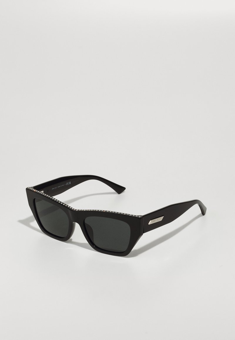 Mustad musta prillid terava kassisilma disainiga, hallid läätsed ja kristallidega kaunistatud raam. Omab tugevaid, nurgelisi käsi dekoratiivse metalllogo'ga.