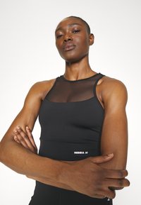 Top atlético negro con una sección superior de malla, diseño ajustado y logotipo de la marca en el dobladillo. Textura suave con tirantes ajustables.