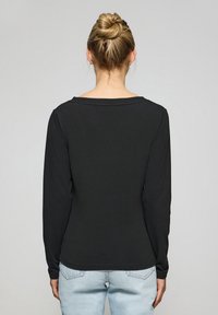 Svart långärmad topp med vid halsringning, tillverkad av ett slätt material, med rak passform och fåll, bärs tillsammans med ljusblå jeans.