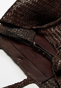Woven dark brown leather tote bag with a textured surface, interior leather lining, and a small strap with silver hardware.