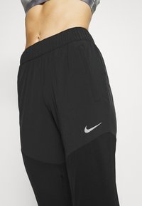 Pantalones deportivos negros con cinturilla elástica, que presentan un logo de Nike gris en el lateral y una textura de tela suave y ligera.