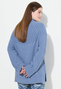 Ljusblått stickat tröja med ribbade och strukturerade mönster, med långa ärmar och en avslappnad passform, avslutad med sidoflikar vid fållen.