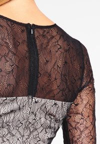 Svart spetsklänning med blommönster, inklusive en genomskinlig övre del och en solid svart bakdragkedja, som kombinerar textur och intrikat design.