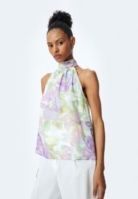 Haut halter en satin avec un motif floral dans des tons pastel de lavande, de vert et de rose. Présente un lien au cou et des épaules dénudées.