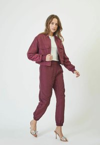 Burgundy cropped bomber jacket with two chest pockets, paired with matching tapered pants and open-toed heels featuring a bow accent.