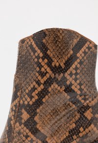 Botín de tobillo con estampado de serpiente marrón y negro, de textura suave, con punta afilada y una costura a lo largo del borde.