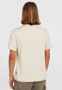 Helles beigefarbenes T-Shirt mit kurzen Ärmeln aus einem strukturierten Stoff, mit rundem Halsausschnitt und einem subtilen seitlichen Nahtdetail.