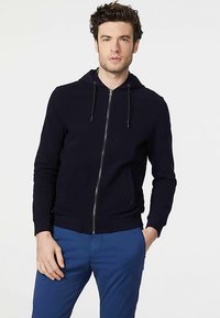 Felpa con cappuccio blu marino con zip, cappuccio con coulisse, tasche frontali e polsini a costine. Realizzata in tessuto morbido con una texture liscia.