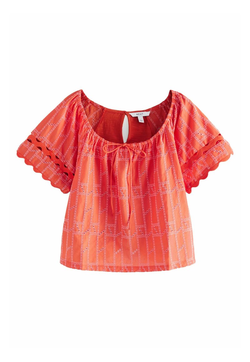Top arancione a maniche corte con schiena scoperta, legatura con coulisse e bordi scallopati. Il tessuto ha una leggera texture a motivi.