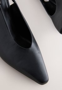 Scarpe con tacco in pelle nera con lato aperto, punta appuntita, texture liscia e dettagli di cuciture minime.