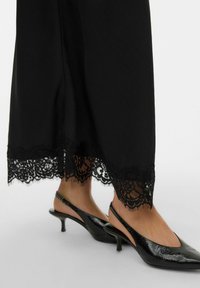 Zwarte enkellange rok met gedetailleerde kanten rand aan de zoom, gecombineerd met elegante zwarte slingback pumps met een puntige neus.