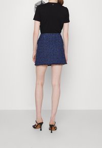 T-shirt noir à manches courtes associé à une mini jupe en tweed bleu avec des franges le long de l'ourlet, portée avec des sandales à talons noires.