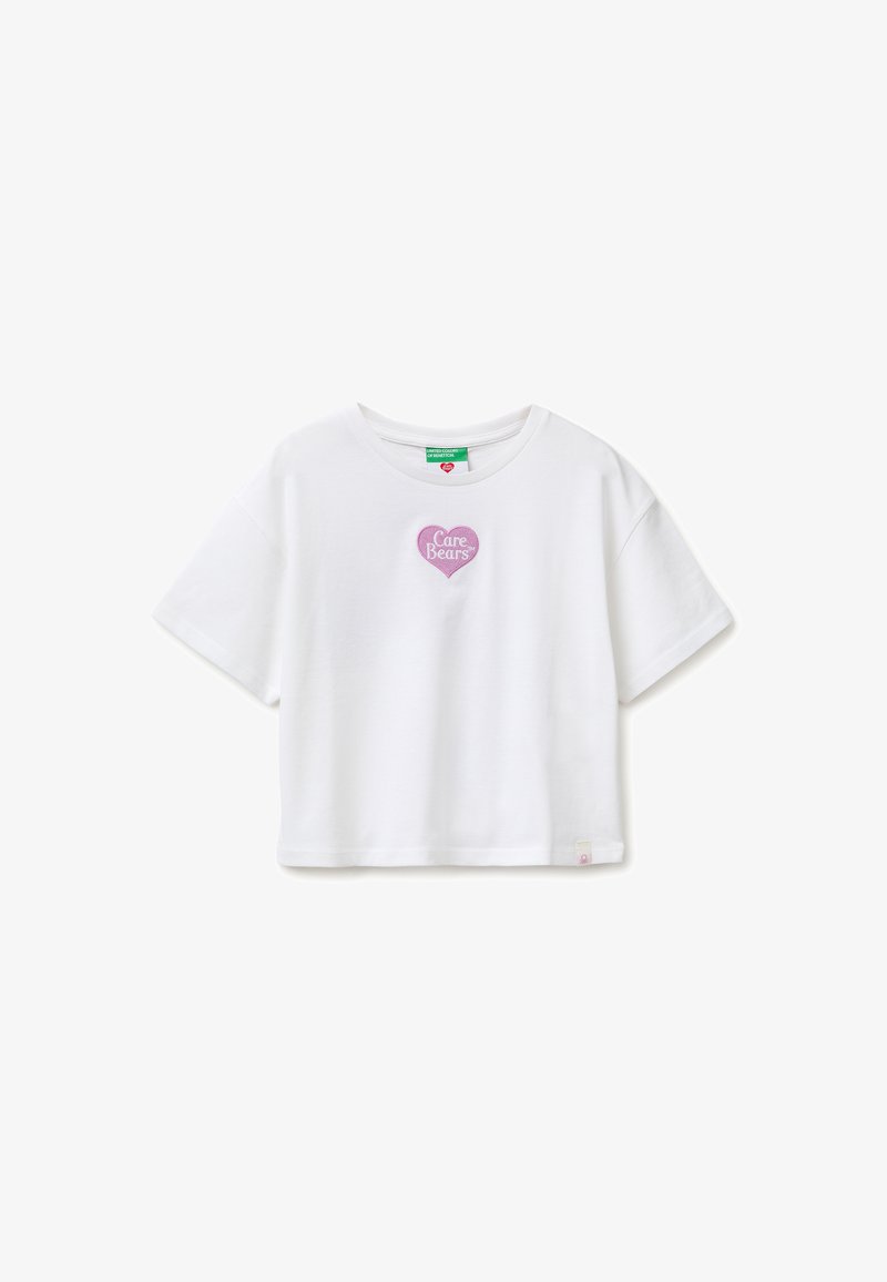 T-shirt blanc court avec manches courtes et un petit patch en forme de cœur rose portant l'inscription « Care Bears » sur la poitrine.