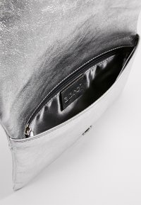 Stříbrná metalická kabelka s hladkým povrchem, se zipovou vnitřní kapsou a značkovým vnitřním štítkem. Čistý design, prostorná.