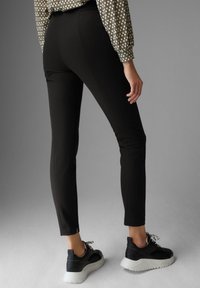 Zwarte aansluitende broeken met een gladde textuur, gecombineerd met zwarte sneakers met witte zolen. De outfit wordt compleet gemaakt met een gebloemde blouse.