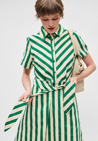 Πράσινο και λευκό ριγέ φόρεμα πουκάμισο με γιακά, κοντά μανίκια, κουμπώματα και δεμένη ζώνη στη μέση. Ομαλή υφή υφάσματος.