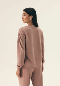 Jasnoróżowy, dzianinowy pulower z okrągłym dekoltem, opuszczonymi ramionami i ściągaczami. W zestawie z pasującymi spodniami, tworząc skoordynowany wygląd.