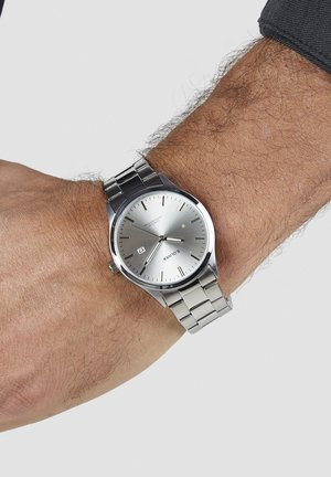 Silver stainless steel watch featuring a minimalist round face, hour markers, and a date display. Metal link bracelet with a polished finish.