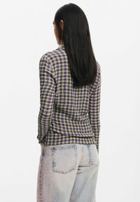 Veste à carreaux en violet, vert et beige. Tissu texturé avec un design ajusté, présentant un ourlet légèrement incurvé et des fentes latérales.