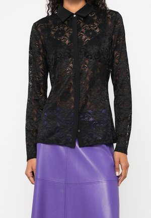 Schwarze, langärmelige durchsichtige Spitzenbluse mit Blumenmustern, getragen über einem violetten Lederrock, zeigt geknöpften Kragen und Frontverschluss.