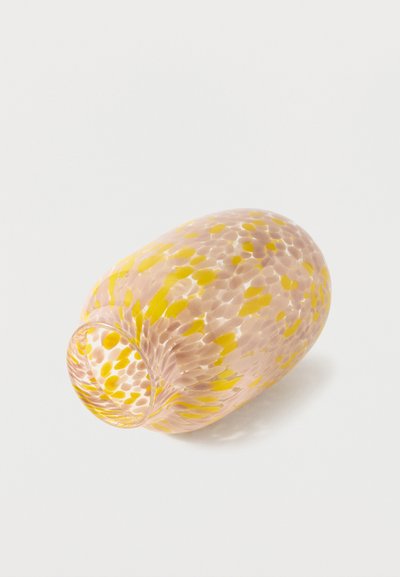 Vase en verre à motifs floraux avec des taches jaunes et rose pâle, couché sur le côté sur un fond blanc.