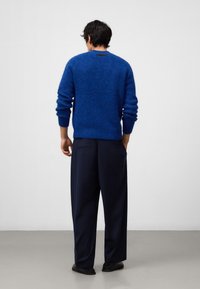 Niebieski, puszysty sweter z dzianiny z okrągłym dekoltem i elastycznymi mankietami, w połączeniu z luźnymi, ciemnymi spodniami. Subtelne logo na plecach.