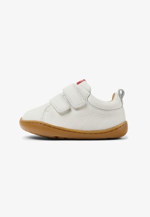 Zapato blanco para niño pequeño con dos tiras de velcro, cuello acolchado, suela de goma marrón y pestaña en el talón, mostrado de lado sobre fondo blanco.