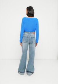 Blue fitted knit sweater with long sleeves paired with light blue wide-leg jeans, featuring a leather back patch and rolled hems.
