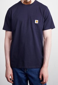 Camiseta de algodón azul marino con un bolsillo en el lado izquierdo del pecho, adornada con un parche de logo cuadrado. Manga corta y corte clásico.