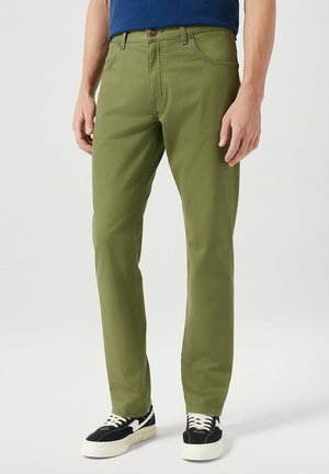Olivengroene katoenen chinos met een rechte pijp, voorzien van zijzakken, een knoopsluiting, en gedragen met zwart-witte sneakers.