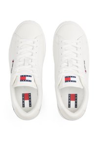 Vita sneakers med en slät läderöverdel, rund tå, platta snören och vadderad tunga. Har märkta etiketter i rött, vitt och blått.