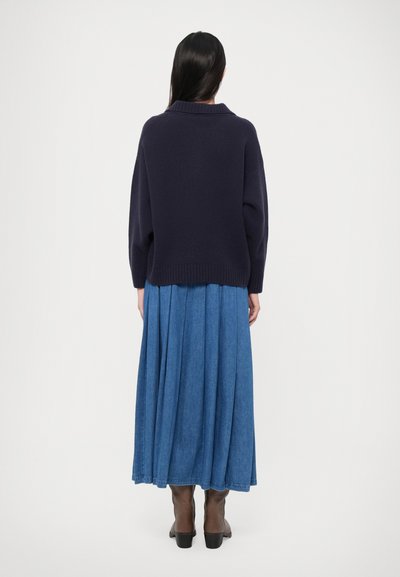 Navy knitted sweater with a ribbed collar paired with a long blue denim skirt. The outfit is complemented by brown ankle boots.
