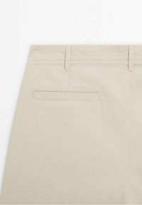 Section de pantalon beige montrant la ceinture arrière avec passants pour ceinture et une poche passepoilée simple.
