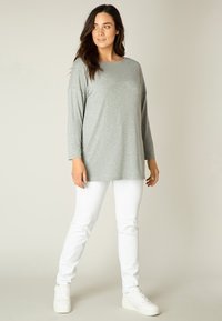 Graues Langarmoberteil mit lässiger Passform, rundem Ausschnitt und weicher Textur, kombiniert mit weißen Slim-Fit-Hosen und weißen Sneakern.