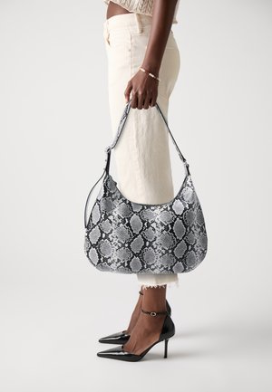 Borsa hobo realizzata in materiale a fantasia di pelle di serpente bianco e nero, con una tracolla singola e una texture liscia. Indossata con pantaloni di colore chiaro.