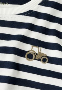 Marineblauw en wit gestreepte stof met een geborduurde bruine tractor op de borst van een kledingstuk.