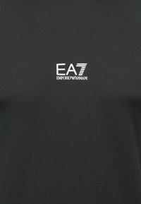 Melns īsroku krekls no gludas auduma. Plūstoša baltā logo "EA7 EMPORIO ARMANI" drukāta uz krūtīm ar treknu fontu.