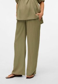 Pantalons larges légers, de couleur vert olive, avec un tissu texturé. Ils offrent une coupe décontractée et des poches latérales, conçus pour le confort et la liberté de mouvement.
