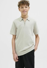 Ljusbeige kortärmad polo i texturerad tyg, med dragkedja vid kragen och en avslappnad passform, tillsammans med svarta byxor.