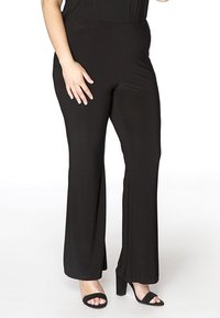 Schwarze Schlaghosen aus glattem, elastischem Material. Mit einem hohen Taillenbund und subtiler Textur. Kombiniert mit schwarzen Absatzsandalen.