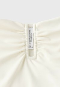 Tissu de vêtement blanc avec un détail froncé autour d'une étiquette cousue indiquant la taille et la marque Stradivarius, fabriqué au Maroc.