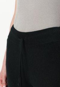 Pantaloni neri di lana con una consistenza morbida, dotati di una vita elastica e di un dettaglio con cordoncino, abbinati a un top grigio a coste.