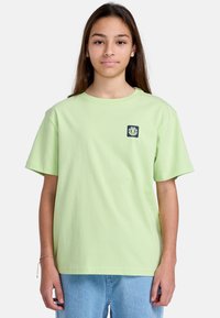 Camiseta de algodón verde claro con mangas cortas, un cuello redondo y un logotipo gráfico azul oscuro en el lado izquierdo del pecho.