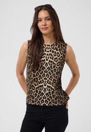 Žena s dugom smeđom kosom koja nosi sunčane naočale na glavi, top bez rukava s uzorkom leoparda i crne hlače, stoji s rukama iza leđa.