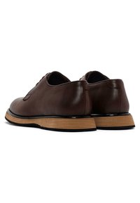 Scarpe da dress in pelle marrone con punta rotonda, caratterizzate da una suola beige rigata e dettagli neri. Il design è fluido con una decorazione minimale.
